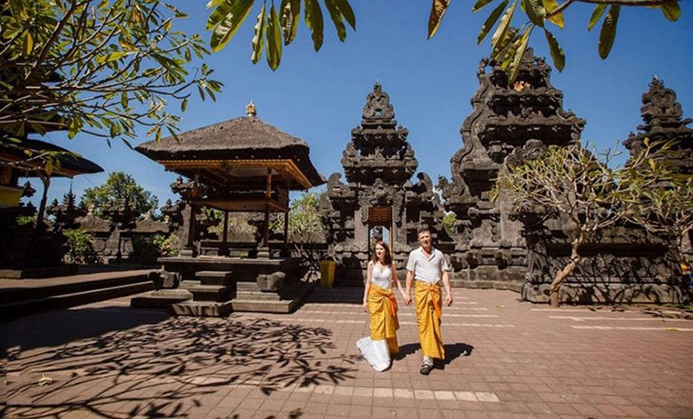 Du khách mặc sarong màu vàng đứng trước cổng đền Besakih với núi Agung phía sau — góc chụp chuẩn nhất Pura Besakih