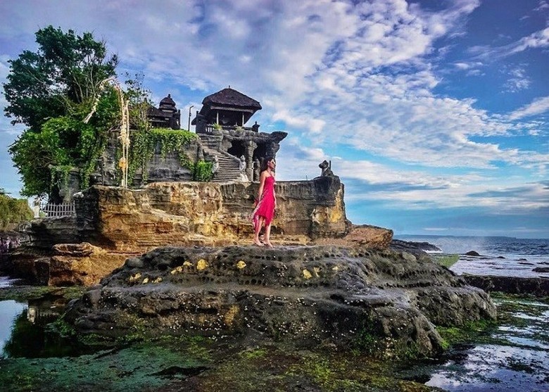 Hoàng hôn Tanah Lot nhìn từ góc thấp, bóng người đứng ngắm phía xa, sóng biển vỗ mạnh vào tảng đá