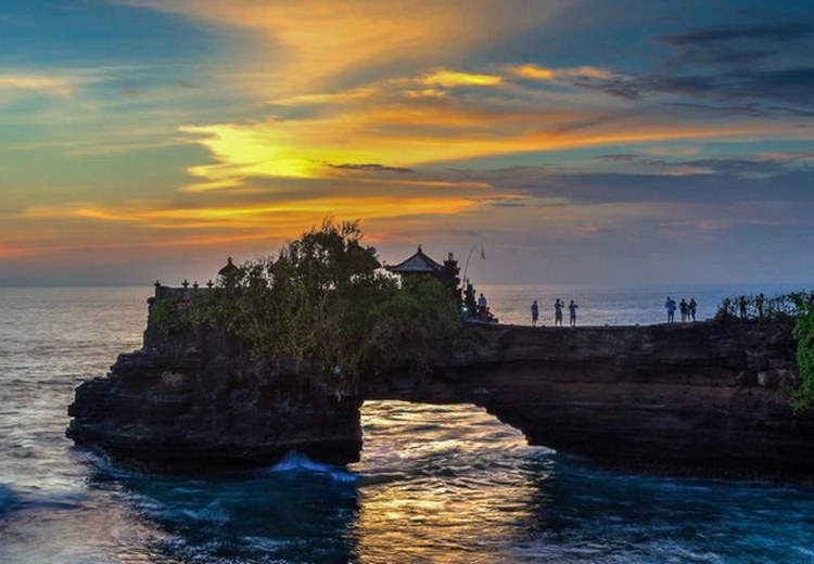 Đền Tanah Lot được chiếu sáng nhẹ, sóng đêm vỗ vào chân đá, bầu trời tím thẫm