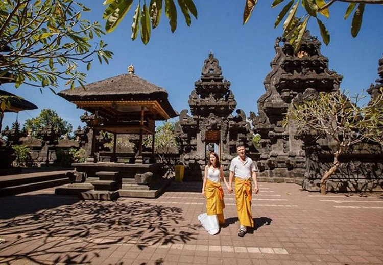 Du khách mặc sarong màu vàng đứng trước cổng đền Besakih với núi Agung phía sau — góc chụp chuẩn nhất Pura Besakih
