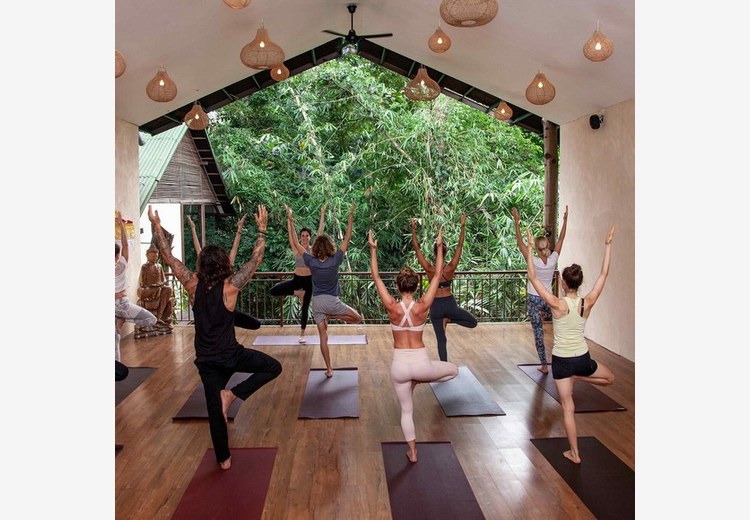 Không gian lớp học yoga ngoài trời tại The Yoga Barn Ubud với sàn gỗ và cây xanh bao quanh