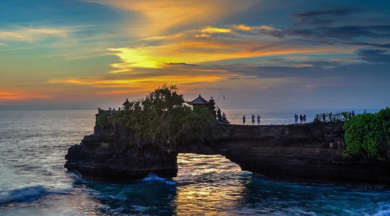 Đền Tanah Lot được chiếu sáng nhẹ, sóng đêm vỗ vào chân đá, bầu trời tím thẫm