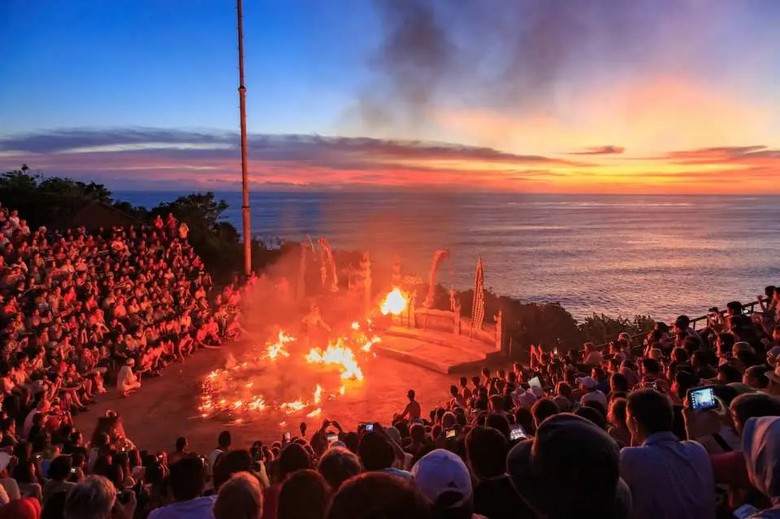 hoàng hôn đỏ rực sau sân khấu múa Kecak tại Uluwatu — cảnh bầu trời và biển phía sau đoàn múa, góc chụp từ khán đài